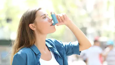 Eine Frau bentutzt einen Inhalator in ihrer Hand.