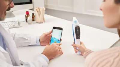 A doctor shows the Vivatmo app to a woman sitting with him, who is holding the Vivatmo device in her hand.